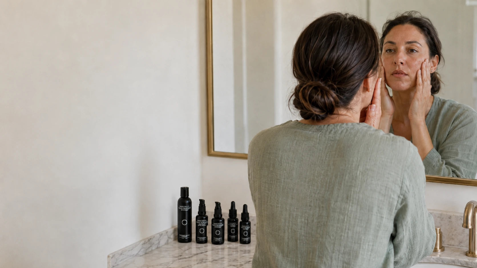 A woman applying skincare at her marble bathroom vanity with a set of Truth Treatment Systems products on the counter, representing the Skin Health Systems collection