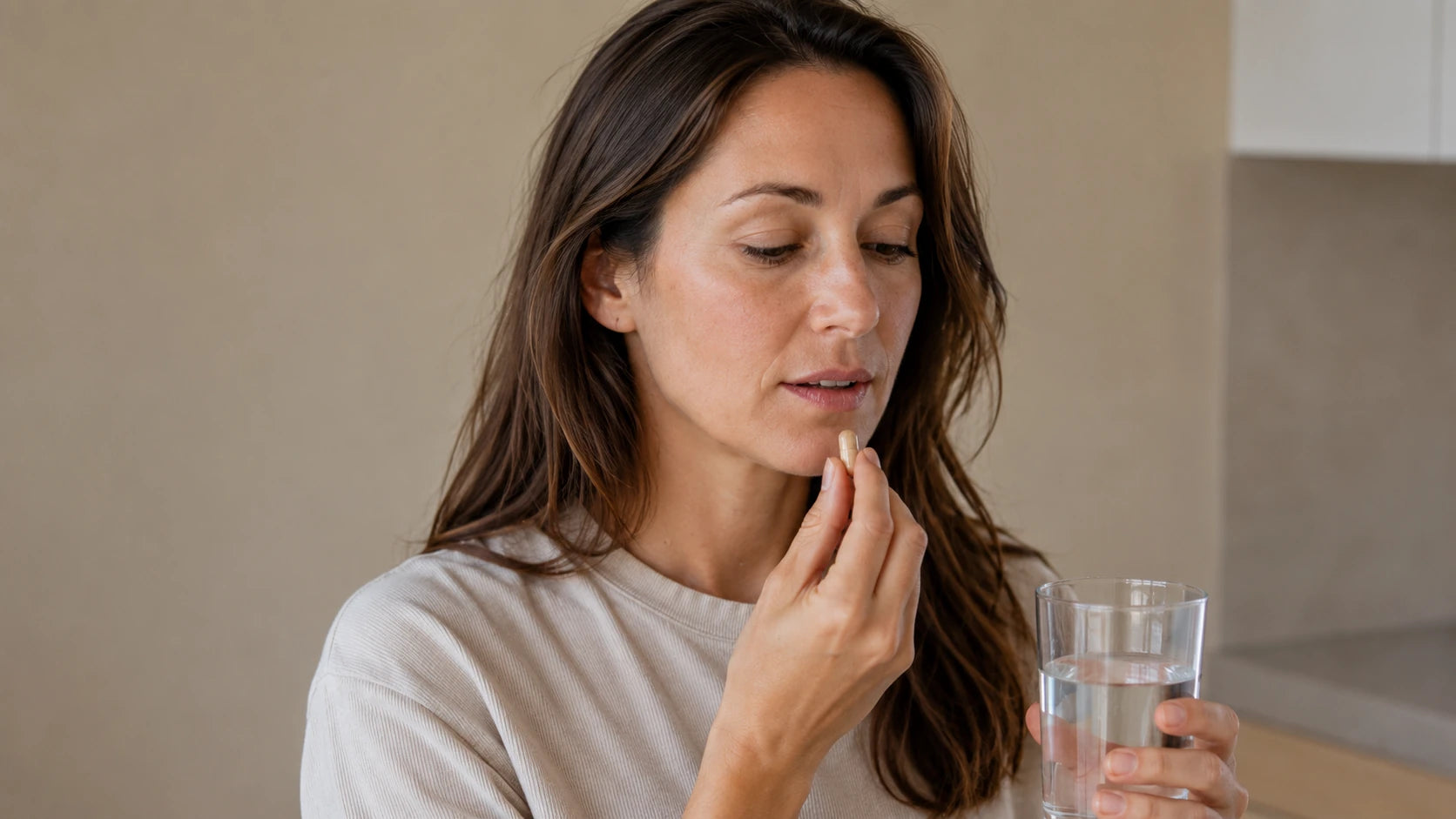 A woman taking a skincare supplement capsule with a glass of water at home, representing Truth Treatment Systems internal skin support